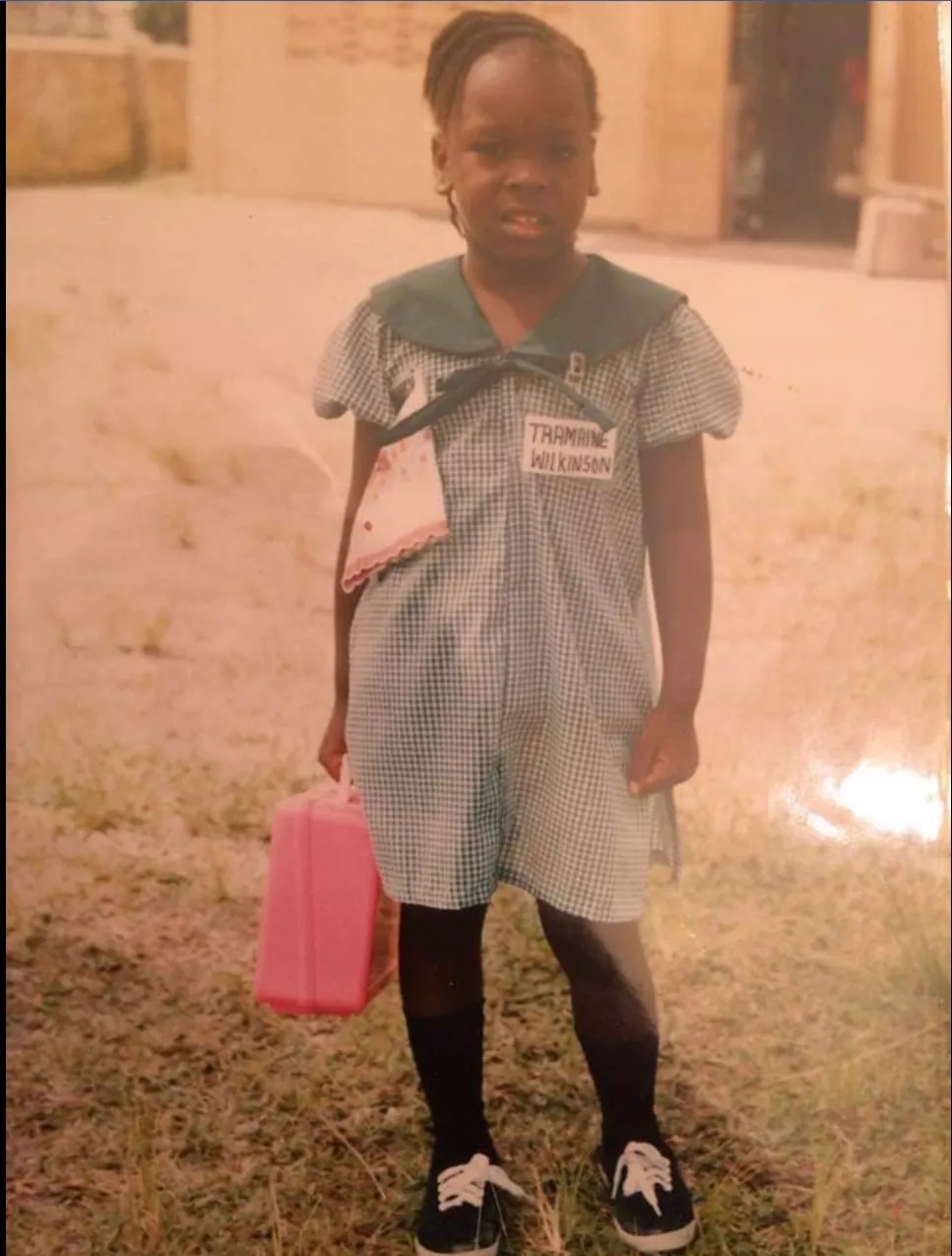 Dr. Tramaine Wilkinson as a young girl in school uniform in Guyana, holding a lunch box